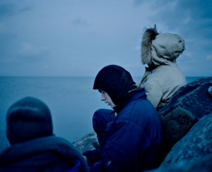 Mathias sits with his friend Trols at the sea shortly after the sun has set. They are outside almost the whole day and enjoy being away from the city. With a group of eight friends they have bought an old sialing boat. They live in a small city at the danish coast where they restore to boat. Next year they want to start sailing the world with it. Photo by Mario Wezel 